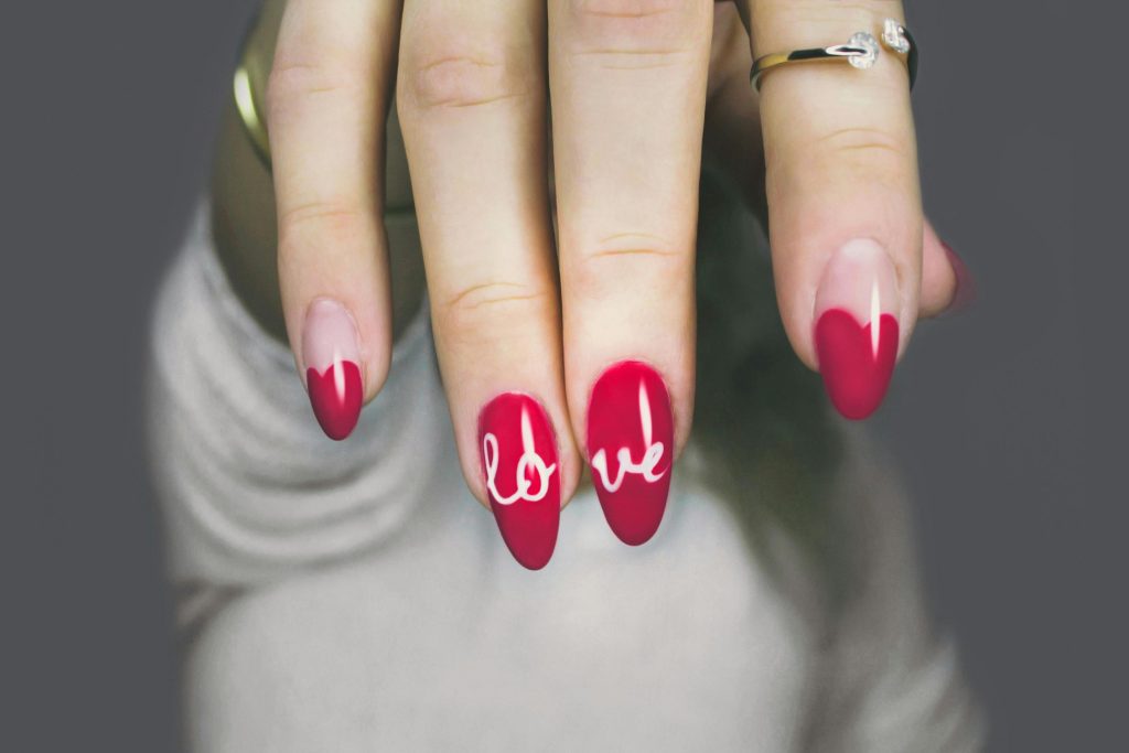 pexels photo 887352 887352 Vibrant red nails with 'love' art on a woman's hand, showcasing elegant style and design.